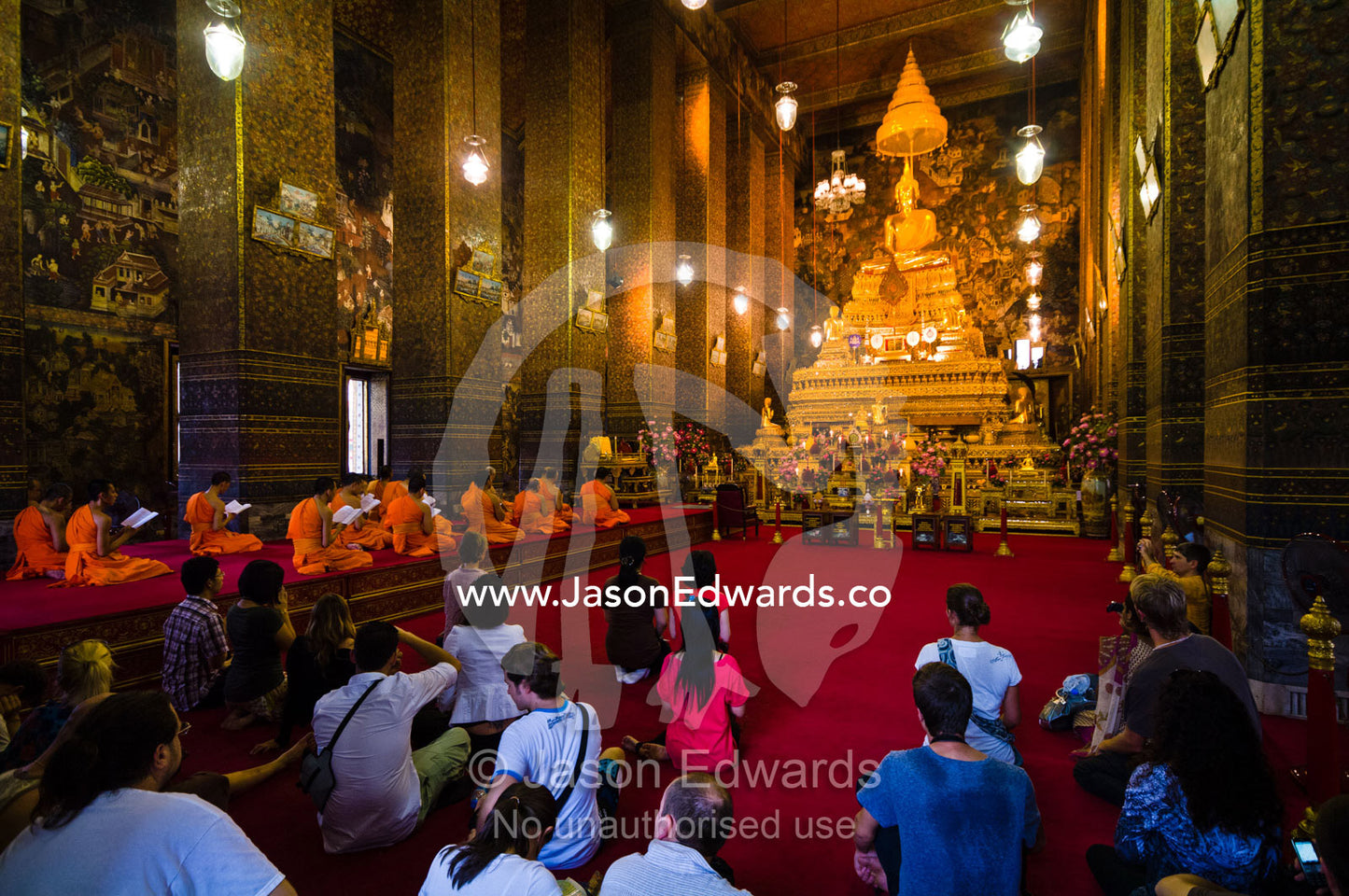 Tourists watch Buddhist monks pray before a golden Buddha in a temple. Wat Pho, Temple of the Reclining Buddha, Wat Chetuphon, Phra Nakhon District, Rattanakosin District, Bangkok, Thailand.