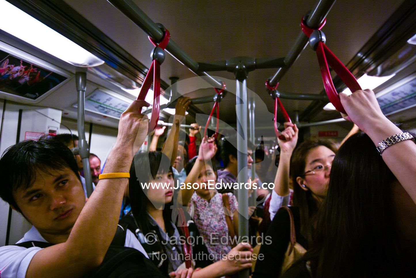 Rush hour commuters watch television to pass the time on a train. Bangkok, Thailand.