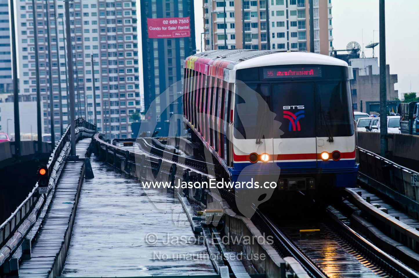 A commuter train approaches a station platform on a rainy day. Bangkok, Thailand.