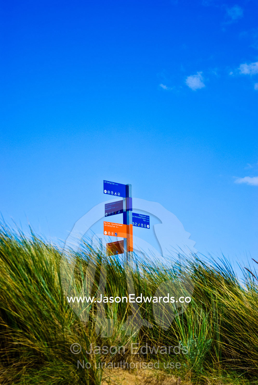 A colourful street sign atop a sand dune for beachside walking trails. Frankston, Port Phillip Bay, Melbourne, Victoria, Australia.