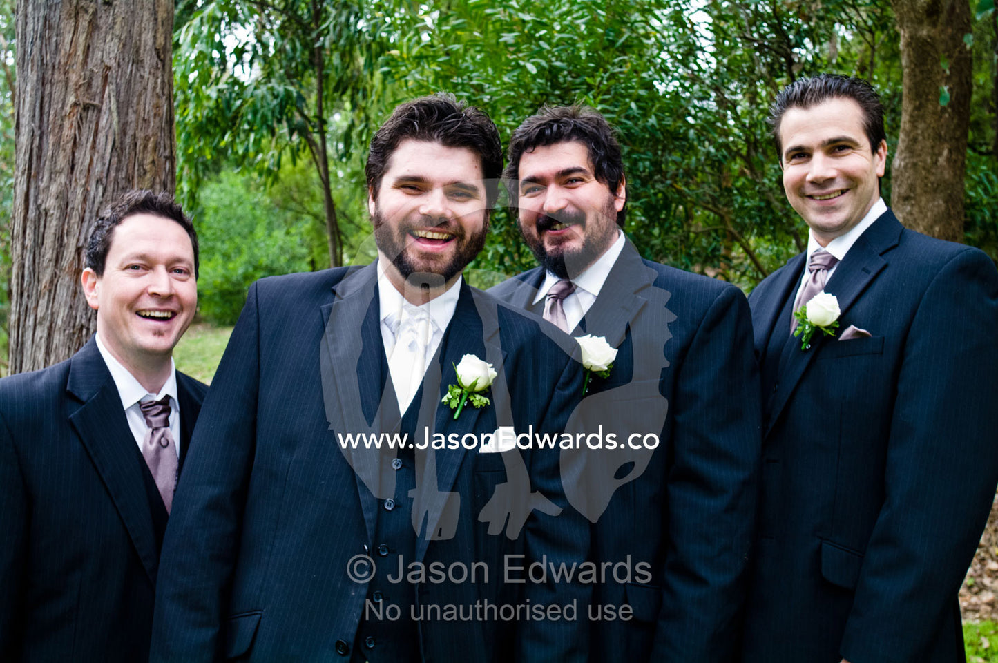 A groom and his groomsmen dressed in suits smiling on his wedding day. Park Orchards, Melbourne, Victoria, Australia.