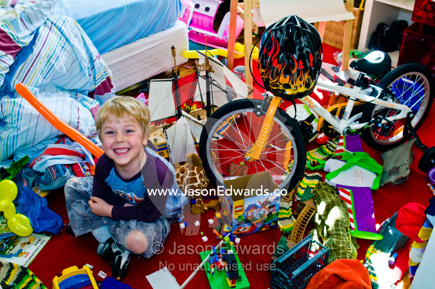 A smiling boy in his messy bedroom surrounded by his toys and bike. North Carlton, Melbourne, Victoria, Australia.