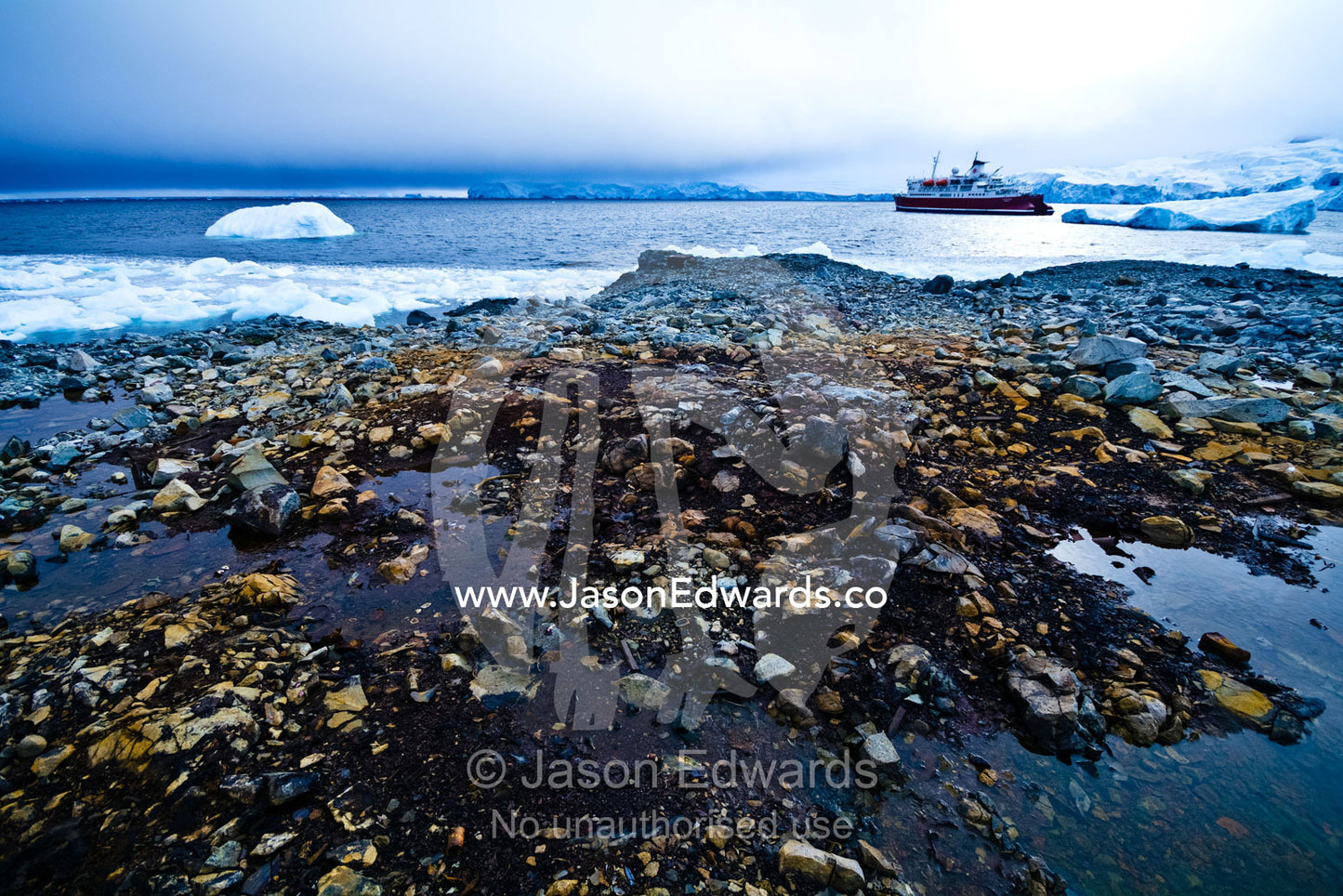 An Antarctic cruise ship anchored in an icy bay off a rocky shore. Prospect Point, Crystal Sound, Antarctic Peninsula, Antarctic Circle, Antarctica.