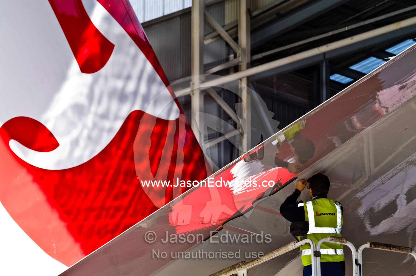 An aeronautical engineer repairs a jet airliner wing from a crane. Kingsford Smith Airport, Mascot, Sydney, New South Wales, Australia.