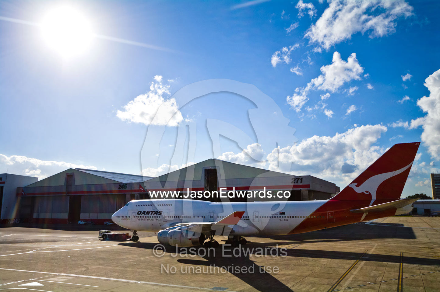 A tractor known as an airplane tug tows a plane across the tarmac. Kingsford Smith Airport, Mascot, Sydney, New South Wales, Australia.