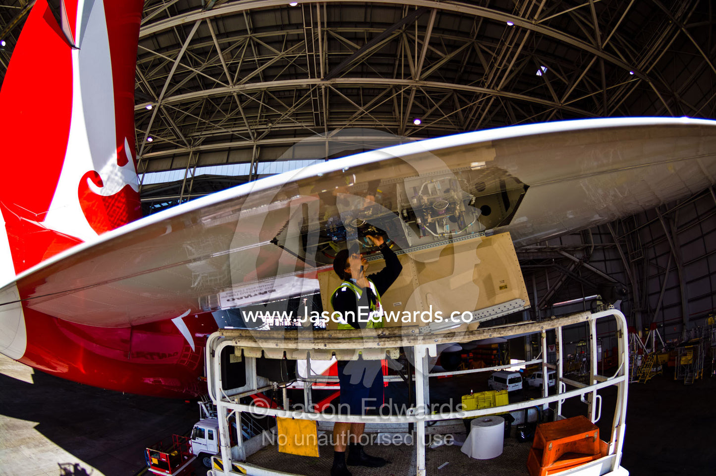 An aeronautical engineer repairs a jet airliner wing from a crane. Kingsford Smith Airport, Mascot, Sydney, New South Wales, Australia.
