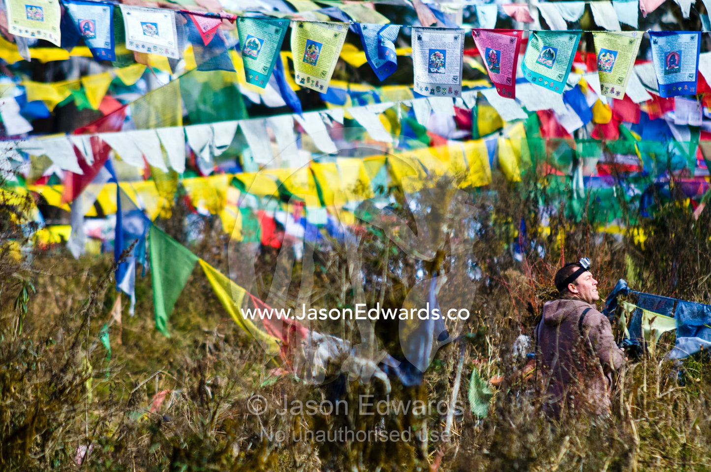 A photographer walks among a canopy of prayer flags on a mountainside. 108 Druk Wangyal Khangzang Chortens, Dochula Pass, Thimphu District, Bhutan.
