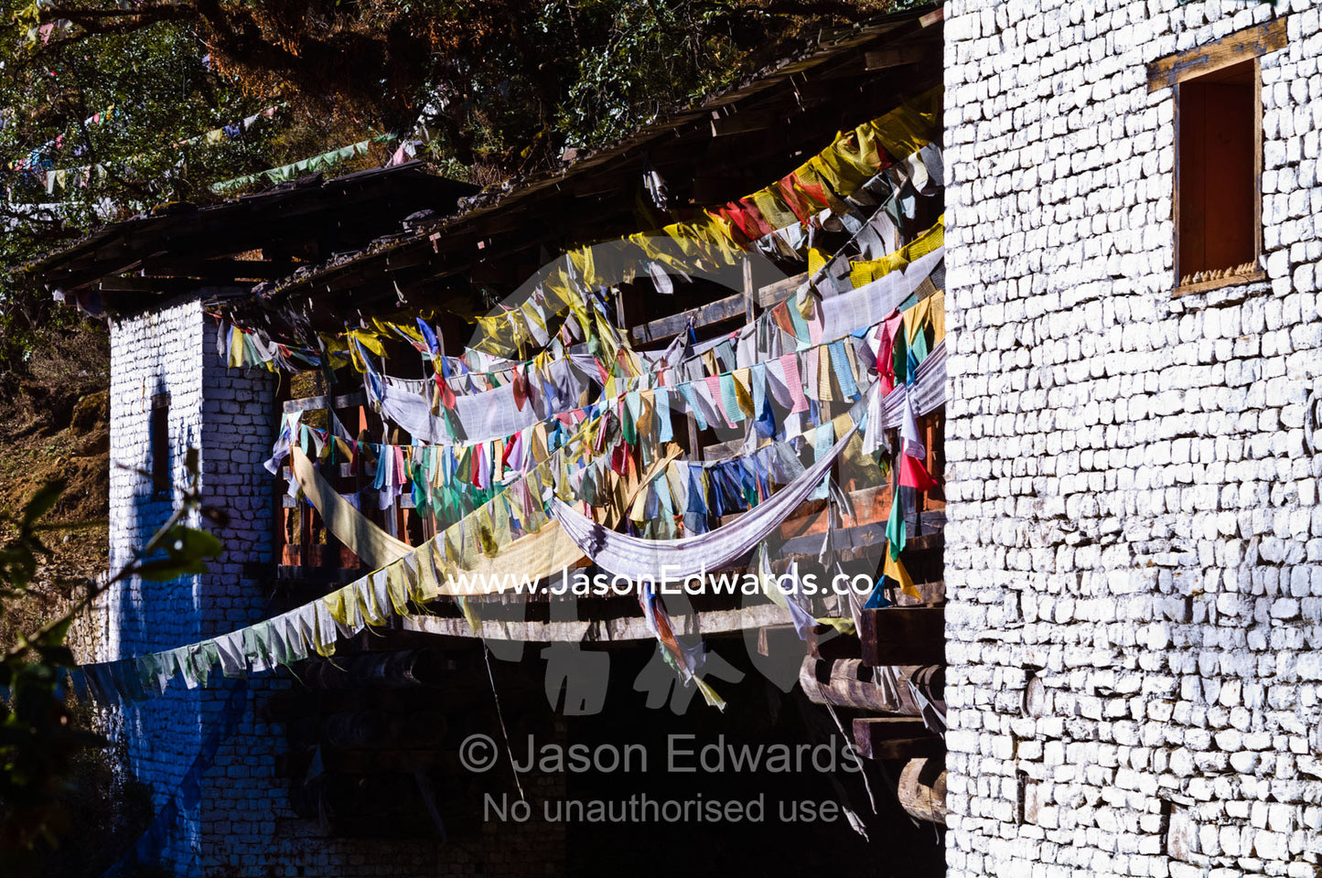 Colorful prayer flags draped across a footbridge between medieval towers near a Buddhist monastery. Jigme Dorji National Park, Cheri Monastery, Chagri Dorjeden Monastery, Thimphu, Thimphu District, Bhutan.