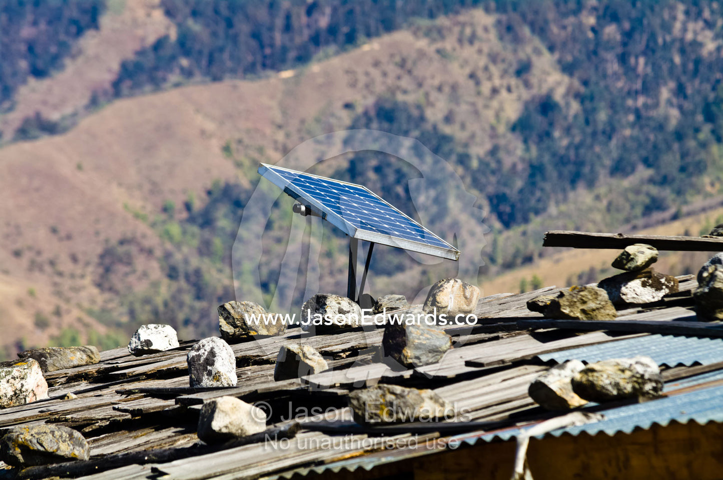 A solar panel generates electricity for a village home with a corrugated tin roof held in place by rocks. Ganteng, Wangdue Phodrang District, Phobjika Valley, Phobjikha Valley, Gangteng Valley, Black Mountains, Bhutan.