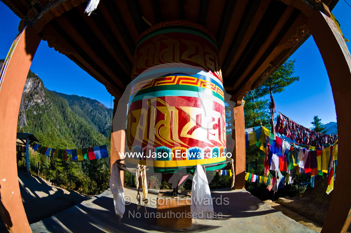 A colorful prayer wheel surrounded by flags on a mountain pass en route to a Buddhist monastery. Paro Taktsang, The Tigers Nest, Paro Valley, Paro District, Bhutan.
