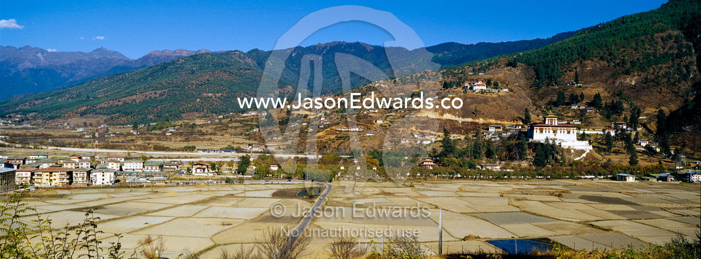 The ancient Paro Dzong overlooking farmland and a town in a wide Himalayan valley. Rinpung Dzong, Paro Dzong, Paro, Paro District, Bhutan.