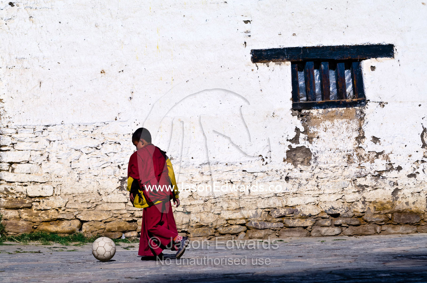 A young Buddhist monk kicks a football around the ancient courtyard of a Buddhist Astrology school. Pangri Zampa Astrology School, Thimphu, Thimphu District, Bhutan.
