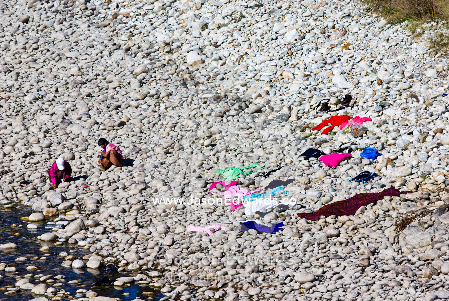Villagers wash their clothes in a Himalayan river and lay them out to dry on the warm stones beside a monastery. Punakha District, Bhutan.