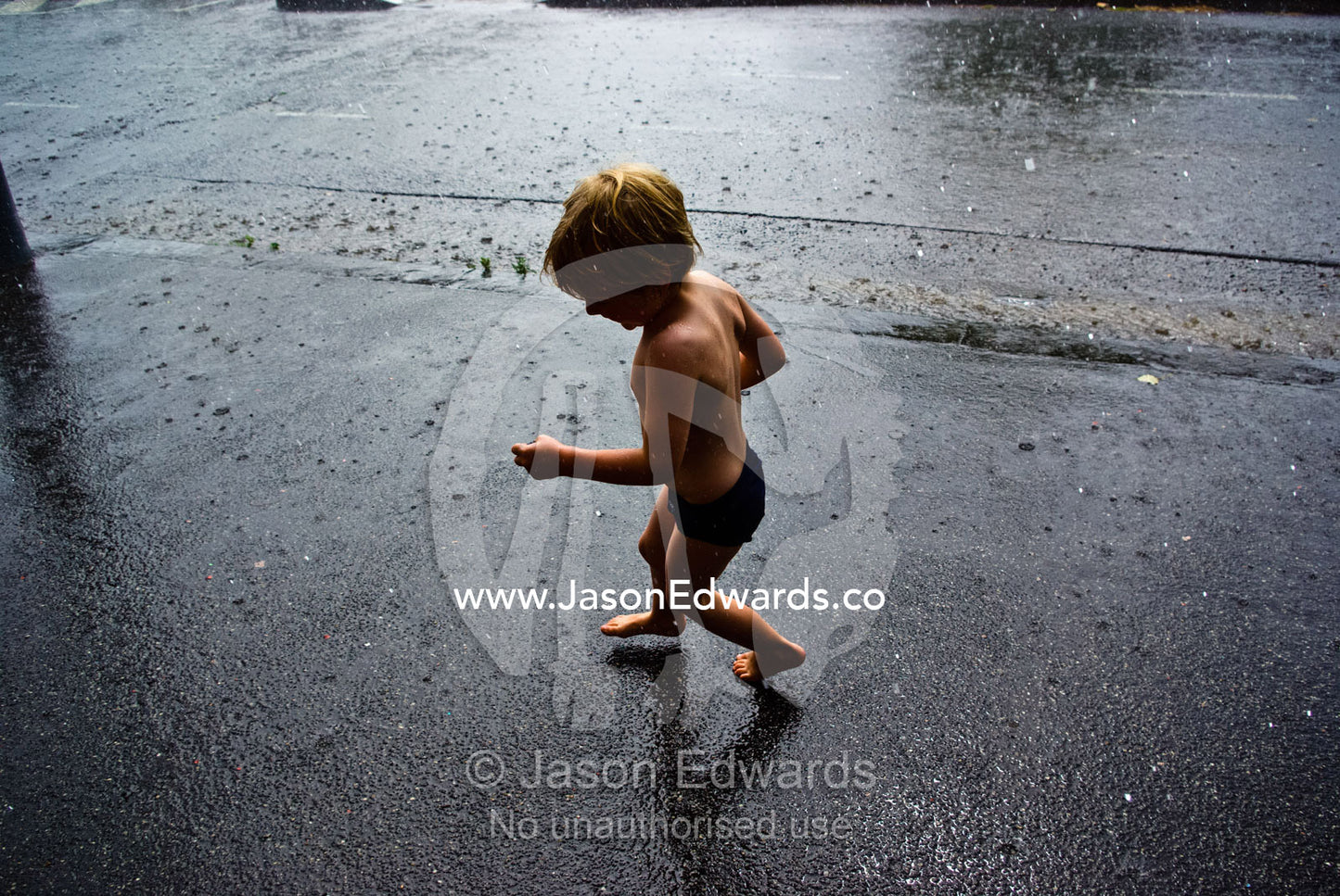 A boy runs around in a summer rain storm downpour on Christmas Day. Carlton North, Melbourne, Victoria, Australia.