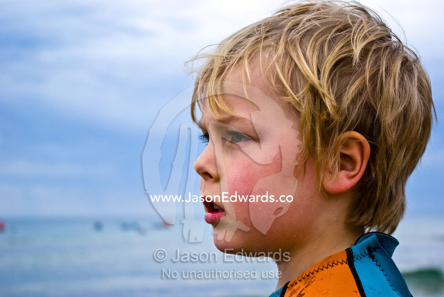 A boy in a wetsuit looks out to sea and the waves on a winters day. Torquay, Surf Coast, Victoria, Australia.