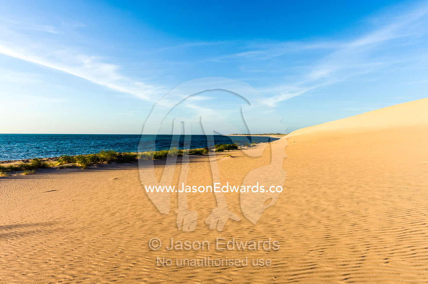 Sweeping coastal desert sand dunes flow into tropical seas at sunset. Cape Range National Park, Exmouth, Ningaloo Reef, Western Australia, Australia.