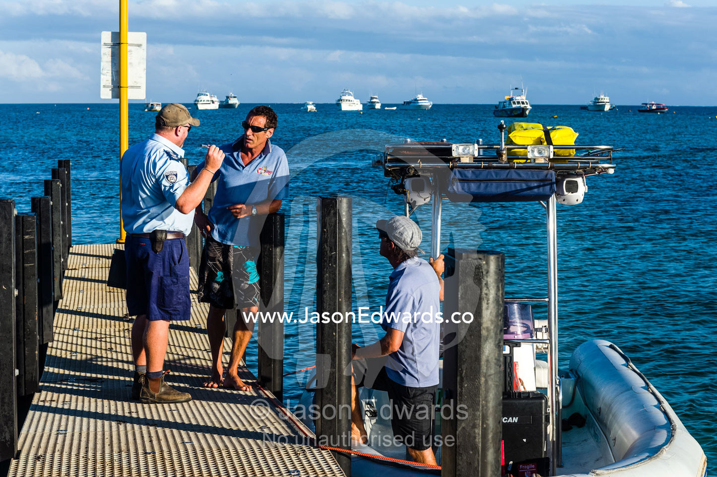 A marine police officer questions a boat captain moored at a jetty. Exmouth, Ningaloo Reef, Western Australia, Australia.