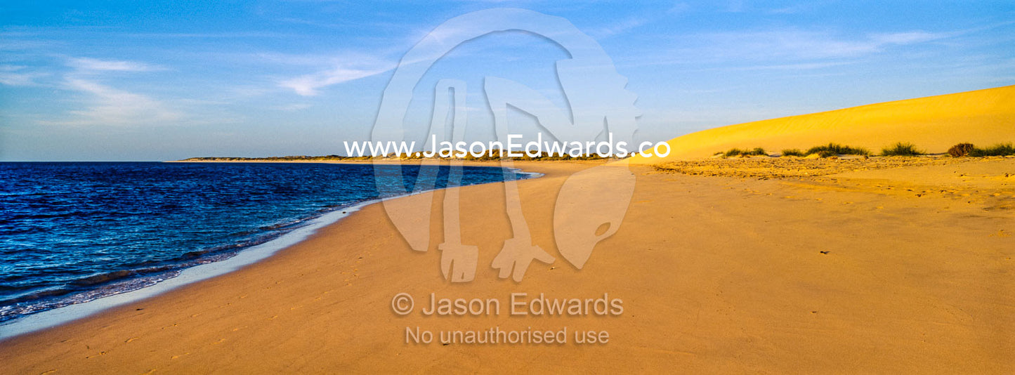 A calm sea laps the shore of a coastal desert sand dune at sunset. Cape Range National Park, Exmouth, Ningaloo Reef, Western Australia, Australia.