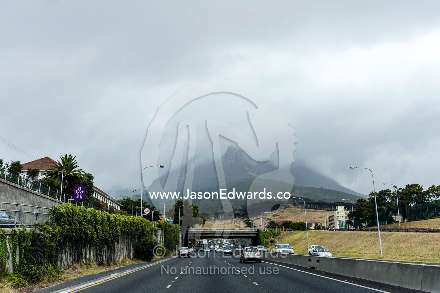 A freeway heads towards mountains shrouded in cloud and rain. Cape Town, Western Cape, South Africa.