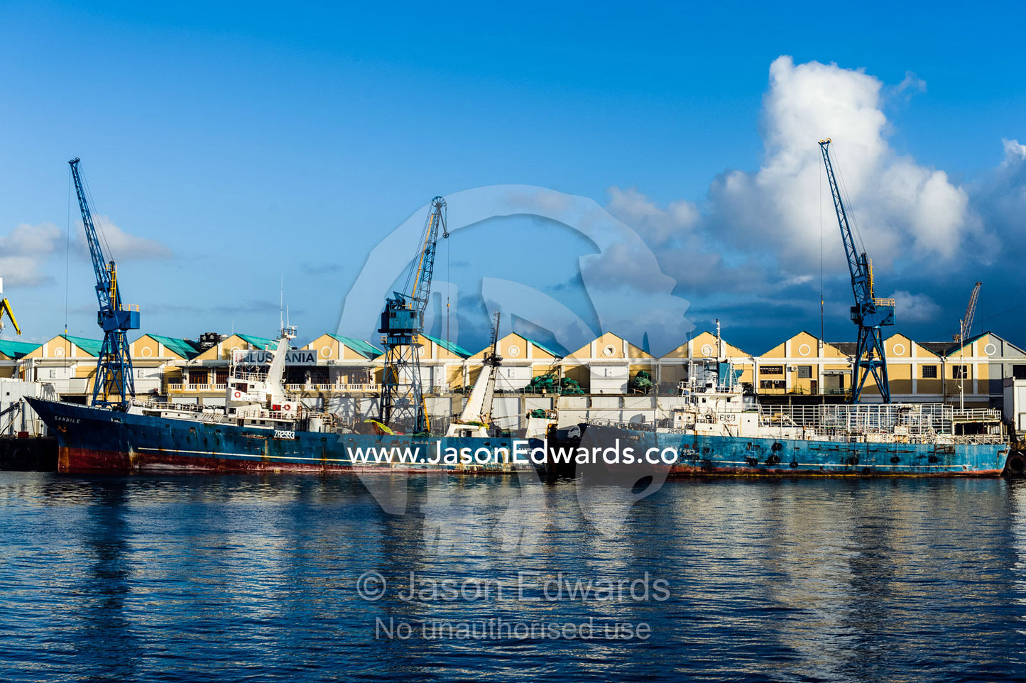 Rusting fishing boats anchored at a factory wharf lined with cranes. Cape Town, Victoria and Alfred Waterfront, Western Cape, South Africa.