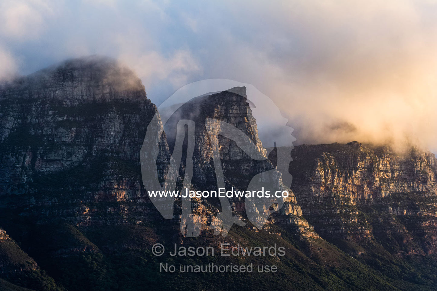 Menacing sunset storm clouds consume a rugged coastal mountain range. The Twelve Apostles, Chapmans Peak Mountain Range, Cape Town, Western Cape, South Africa.