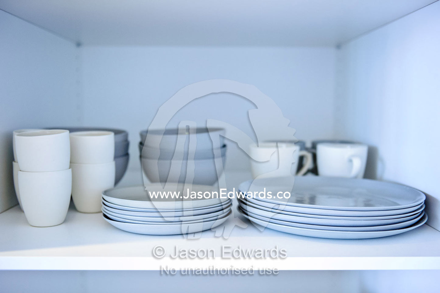 White porcelain plates, cups and bowls in a city apartment cupboard. North Melbourne, Melbourne, Victoria, Australia.