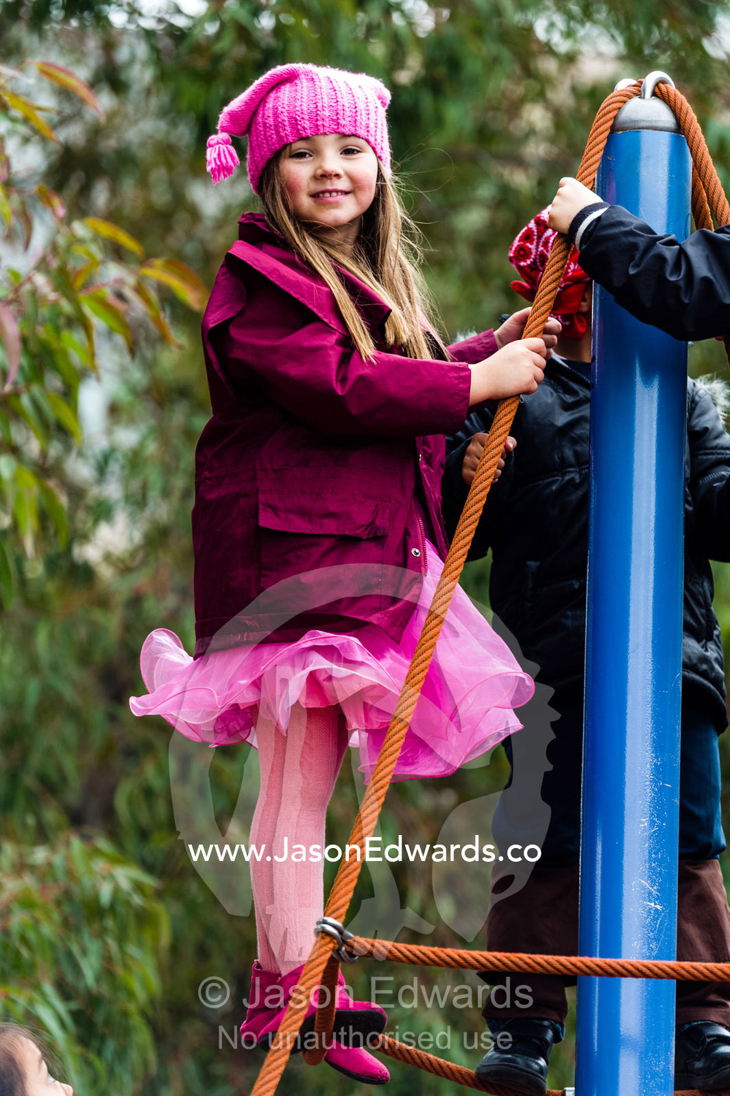 A schoolgirl proudly stands at the summit of a rope climbing frame. Birrarung Marr Park, Federation square, Melbourne, Victoria, Australia.