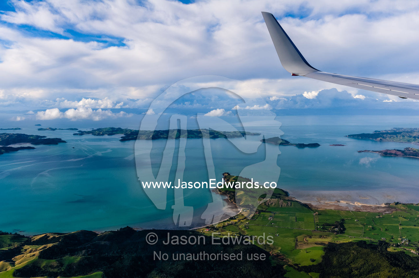 A passenger jet flying over a beautiful coastline and turquoise bay. Auckland, New Zealand.