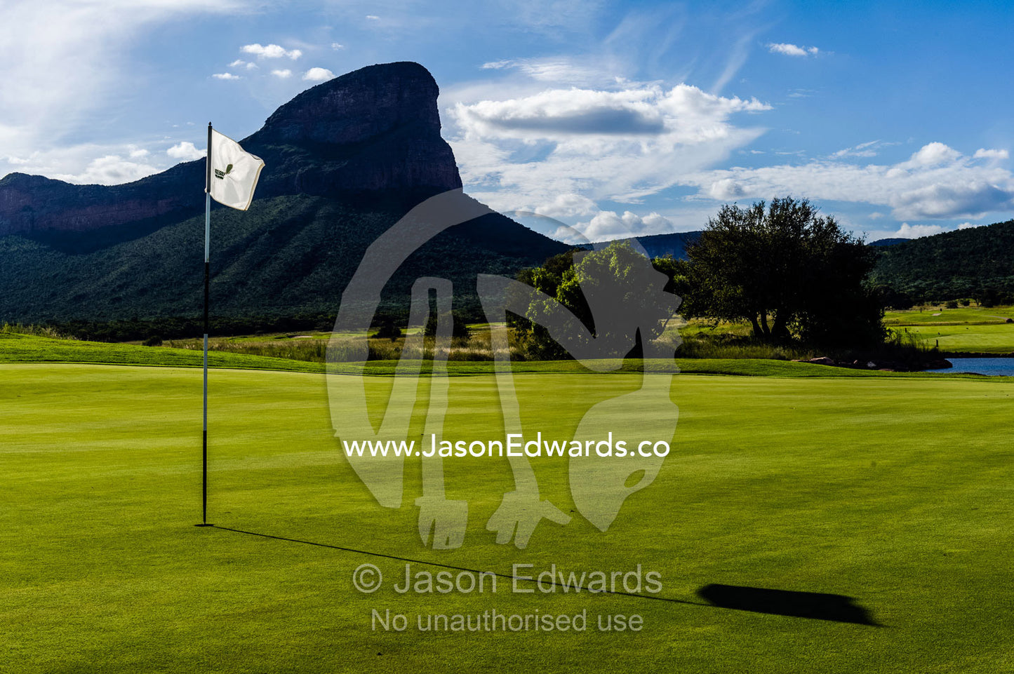 A flag rests in the cup on a golf green beneath rugged mountain peaks. Legend Golf Safari Resort, Waterberg Mountains, Entabeni Game Reserve, Limpopo Province, South Africa.