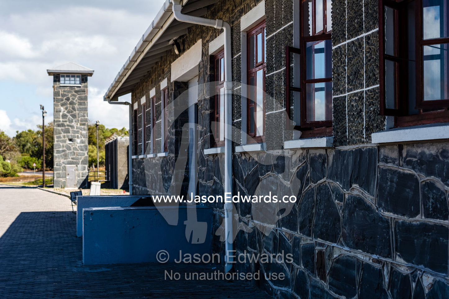 A prison wall patrolled by a bluestone guard tower. Cape Town, Robben Island, Bloubergstrand, Table Bay, Western Cape, South Africa.