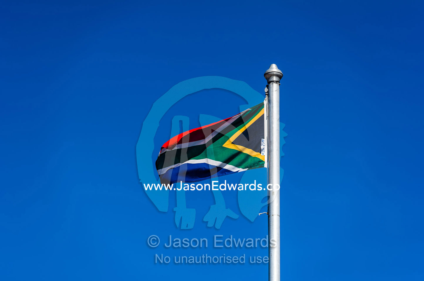 The South African flag fluttering in a clear blue sky above a prison. Cape Town, Robben Island, Bloubergstrand, Table Bay, Western Cape, South Africa.
