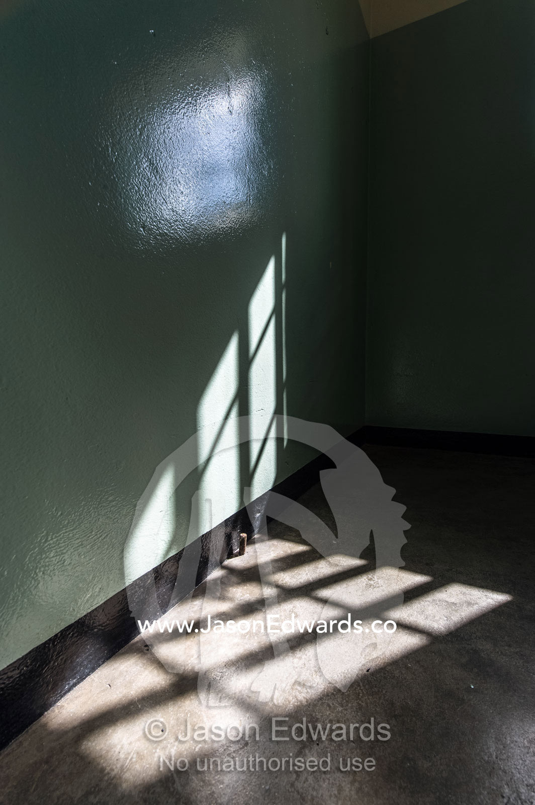 Sun rays cast window bar shadows into Nelson Mandela's prison cell. Robben Island, Cape Town, Bloubergstrand, Table Bay, Western Cape, South Africa.