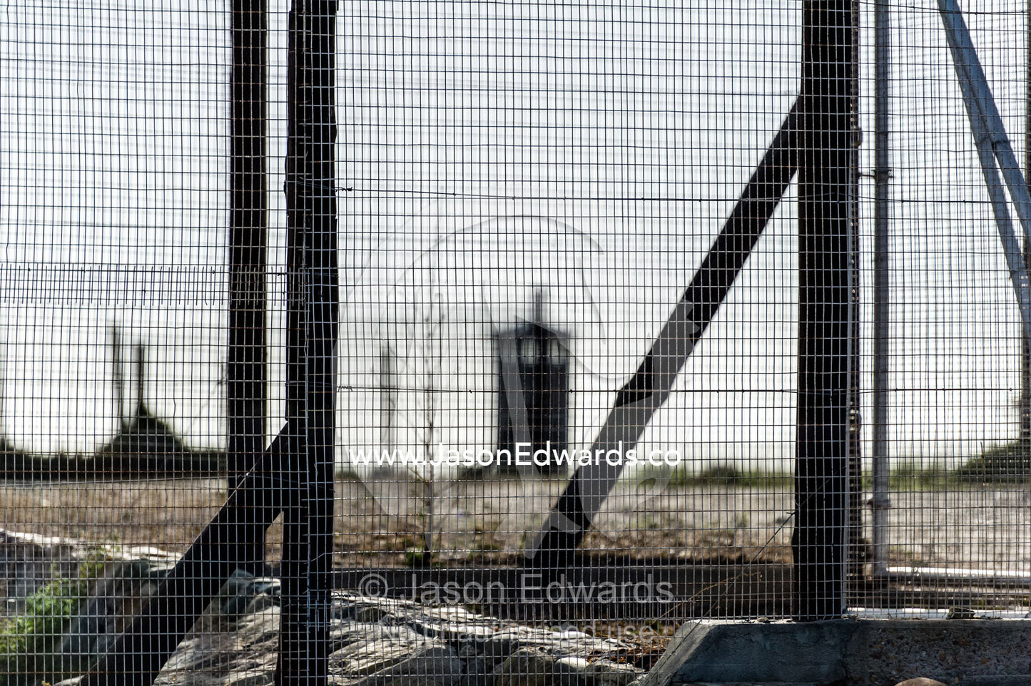 Rows of steel and wire mesh fencing surround a prison and guard tower. Robben Island, Cape Town, Bloubergstrand, Table Bay, Western Cape, South Africa.