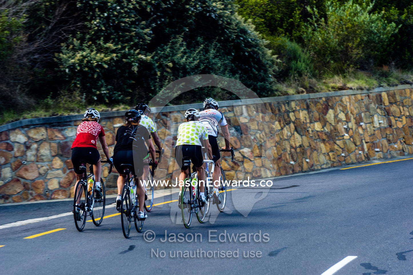 Cyclists speed down a winding coastal road on their racing bikes. Cape Town, Chapmans Peak Drive, Chapmans Peak, Western Cape, Cape Peninsula, South Africa.