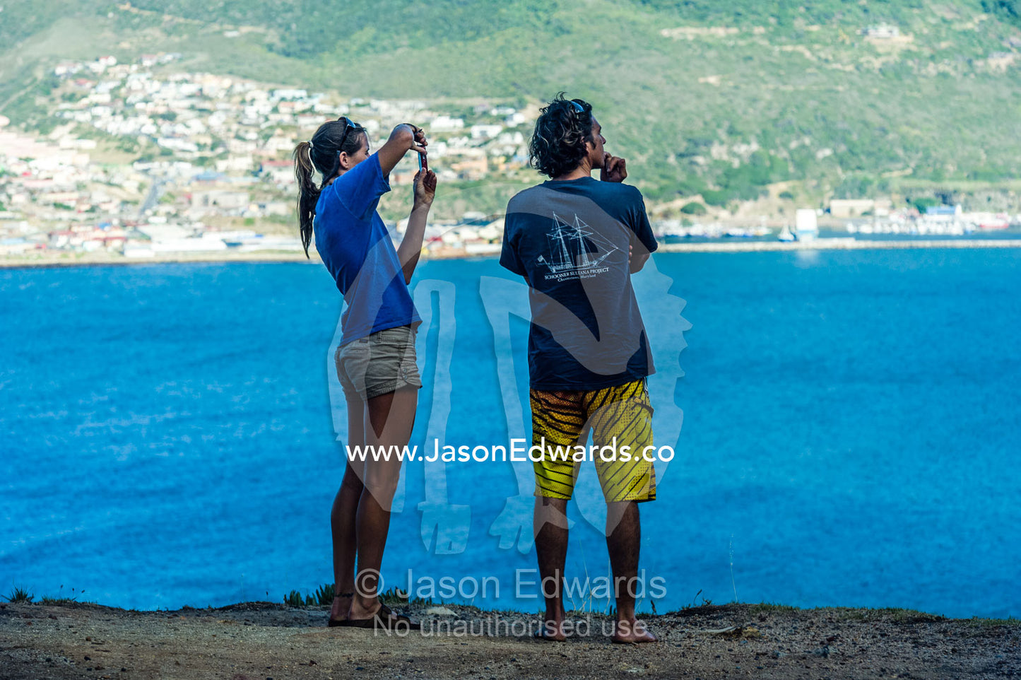 Tourists photograph a picturesque bay from a cliff over the ocean. Hout Bay, Cape Town, Chapmans Peak Drive, Western Cape, Cape Peninsula, South Africa.