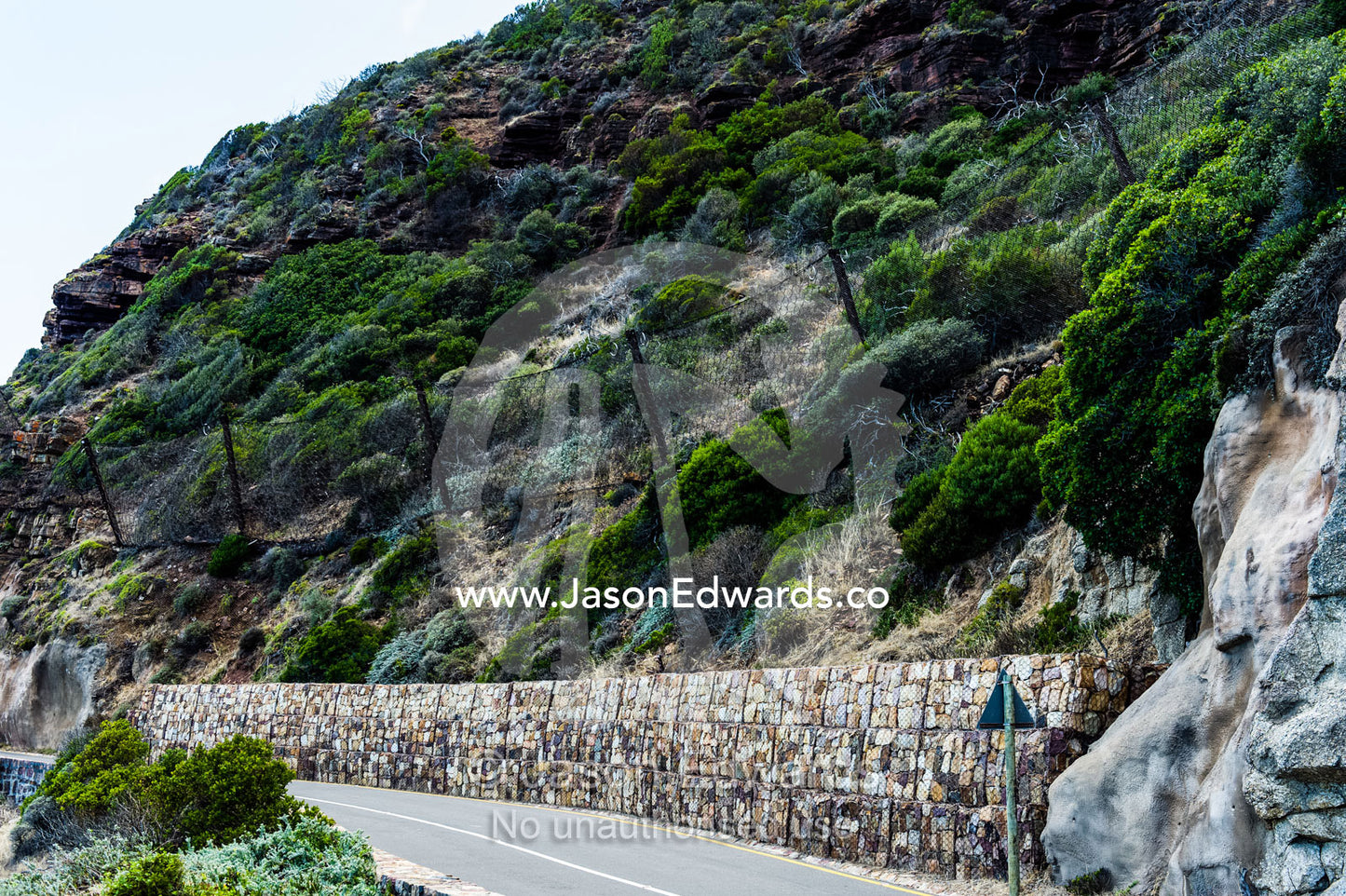 Wire mesh netting catches boulders that fall from a cliff onto a road. Cape Town, Chapmans Peak Drive, Chapmans Peak, Western Cape, Cape Peninsula, South Africa.