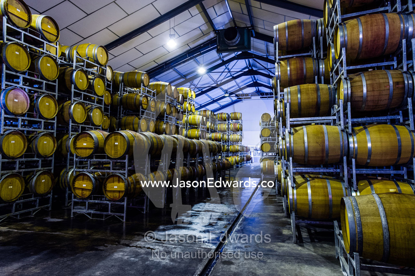 Racks holding rows of wine barrels in a winery storage warehouse. Fairview Wine Estate, Stellenbosch, Western Cape, South Africa.