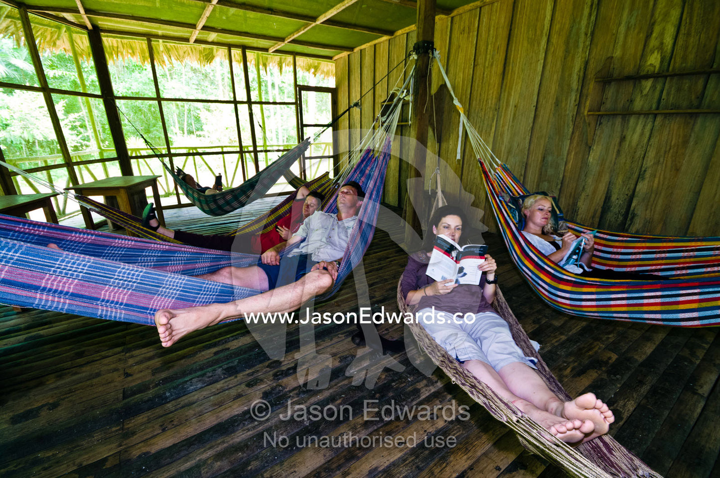 Tourists and conservation volunteers relaxing and reading in hammocks in a lodge in the Amazon rainforest. Amazon Basin, Loreto Region, Maynas Province, Peru.