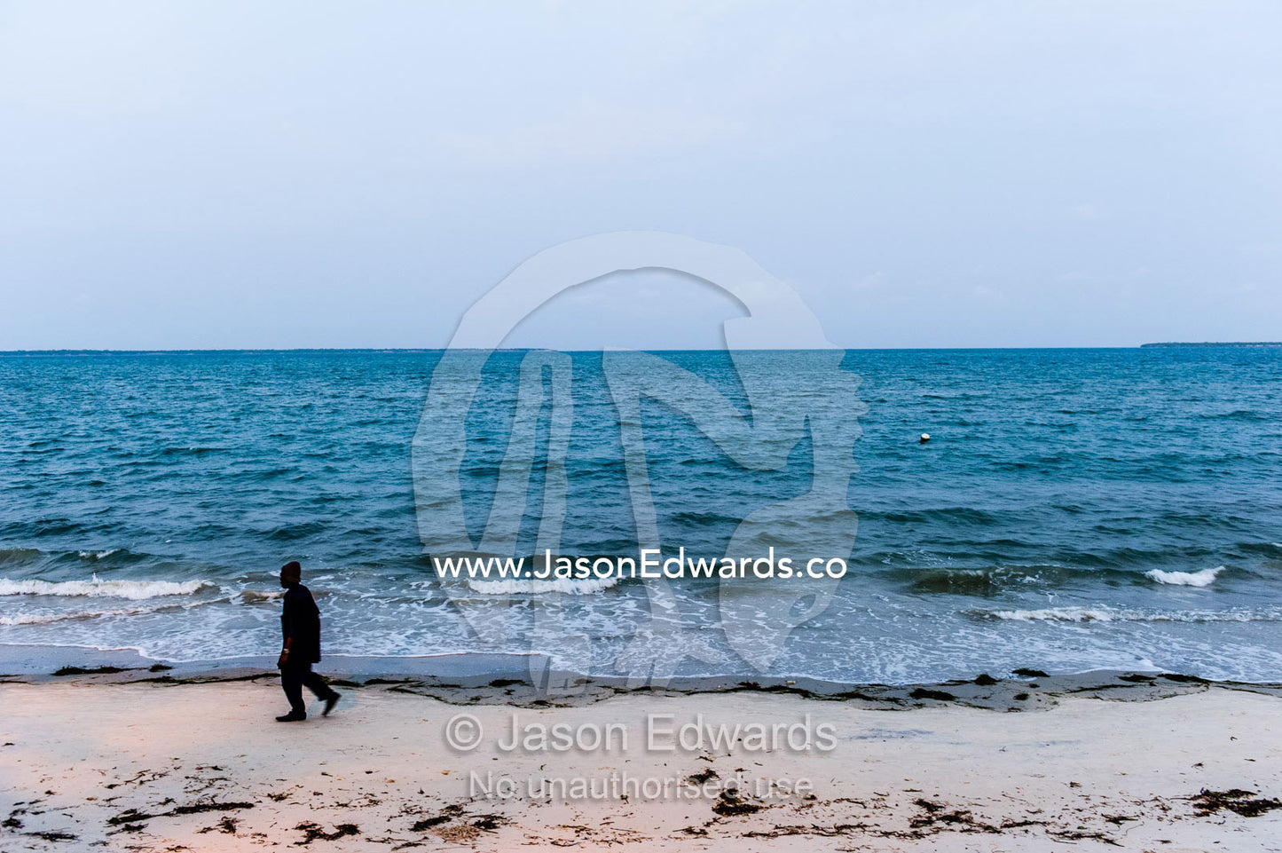 A man walking along an empty beach after finishing work at sunset. Dar es Salaam, Kawe, Tanzania, Africa.