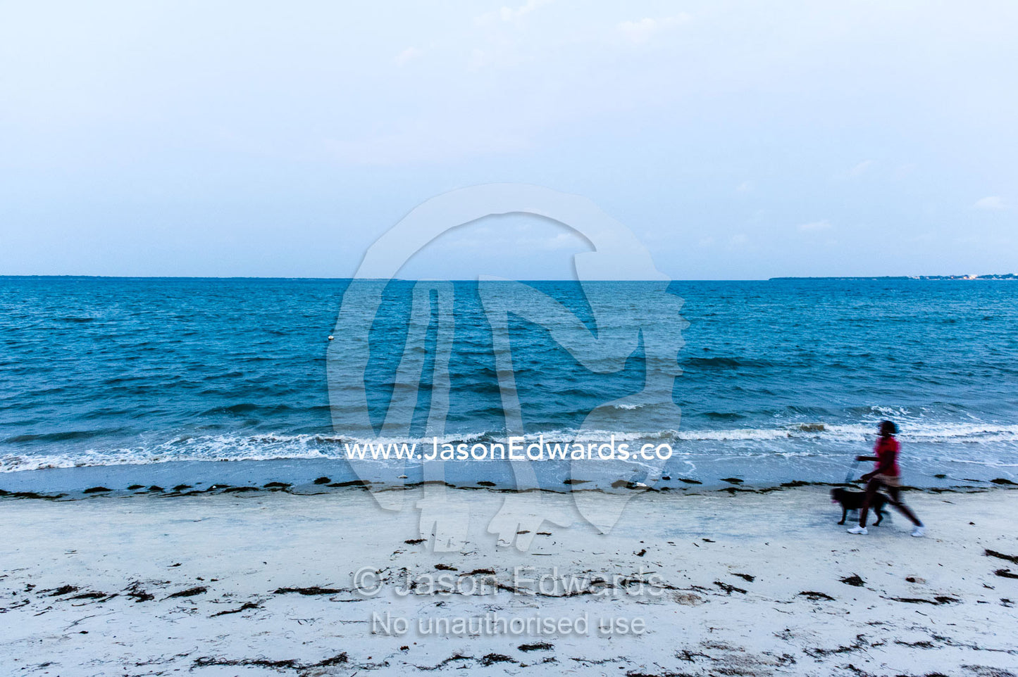 A lady walking her dog along an empty beach after sunset. Dar es Salaam, Kawe, Tanzania, Africa.