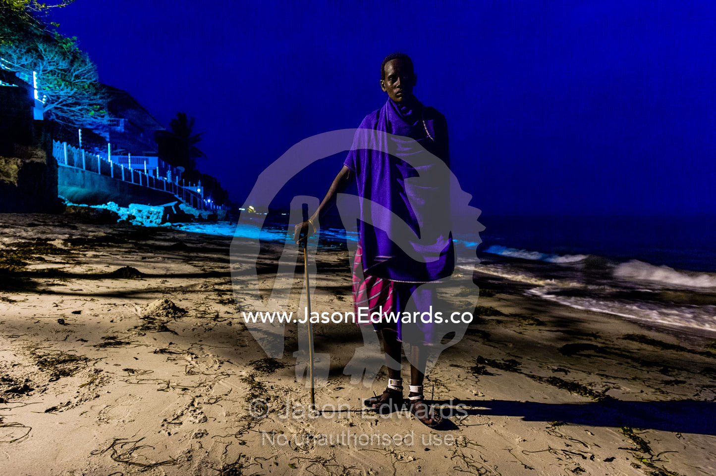 A young Masai warrior lured to the city waits to entertain guests at a seaside hotel. Dar es Salaam, Kawe, Tanzania, Africa.