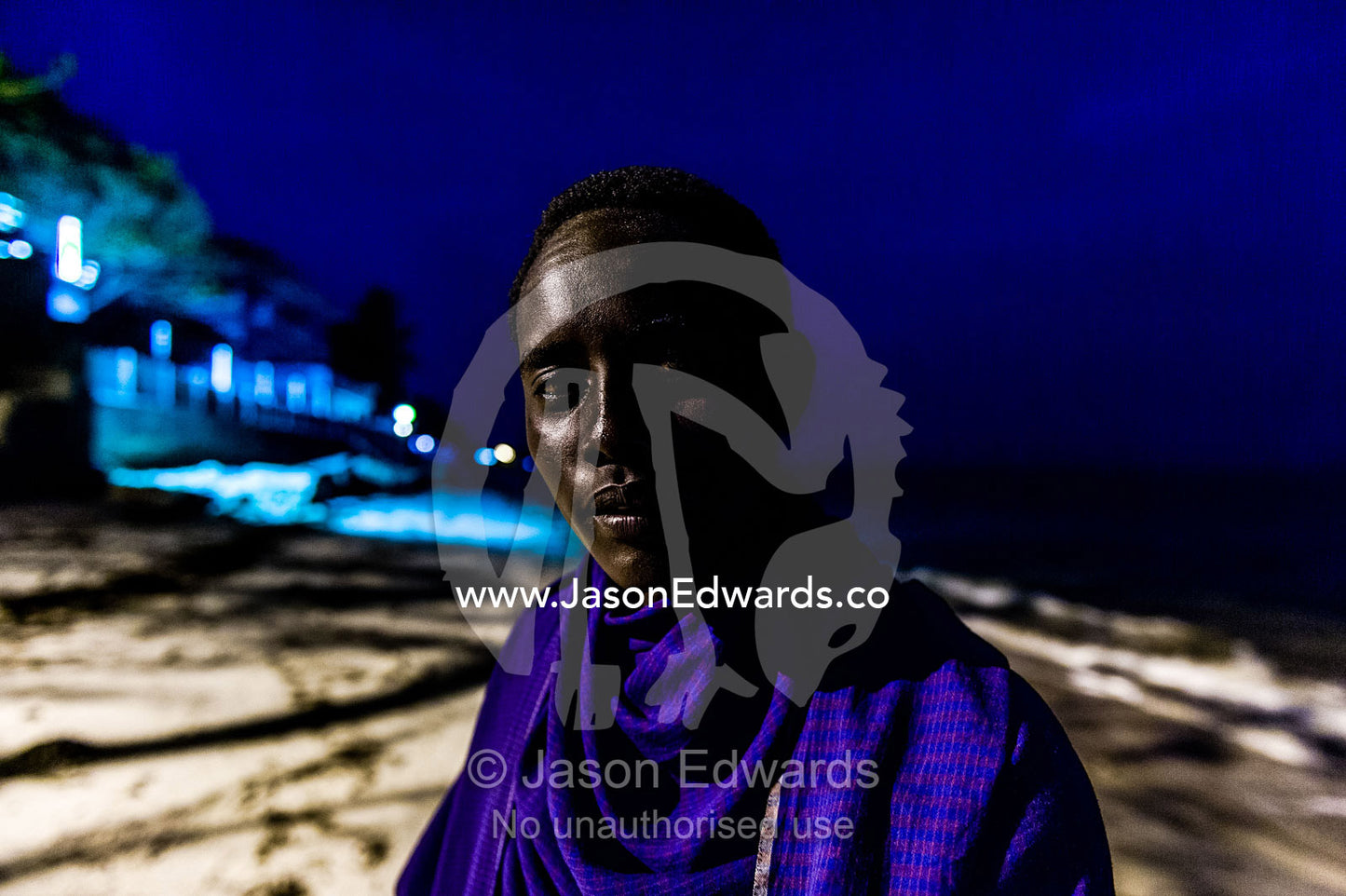A young Masai warrior lured to the city waits to entertain guests at a seaside hotel. Dar es Salaam, Kawe, Tanzania, Africa.