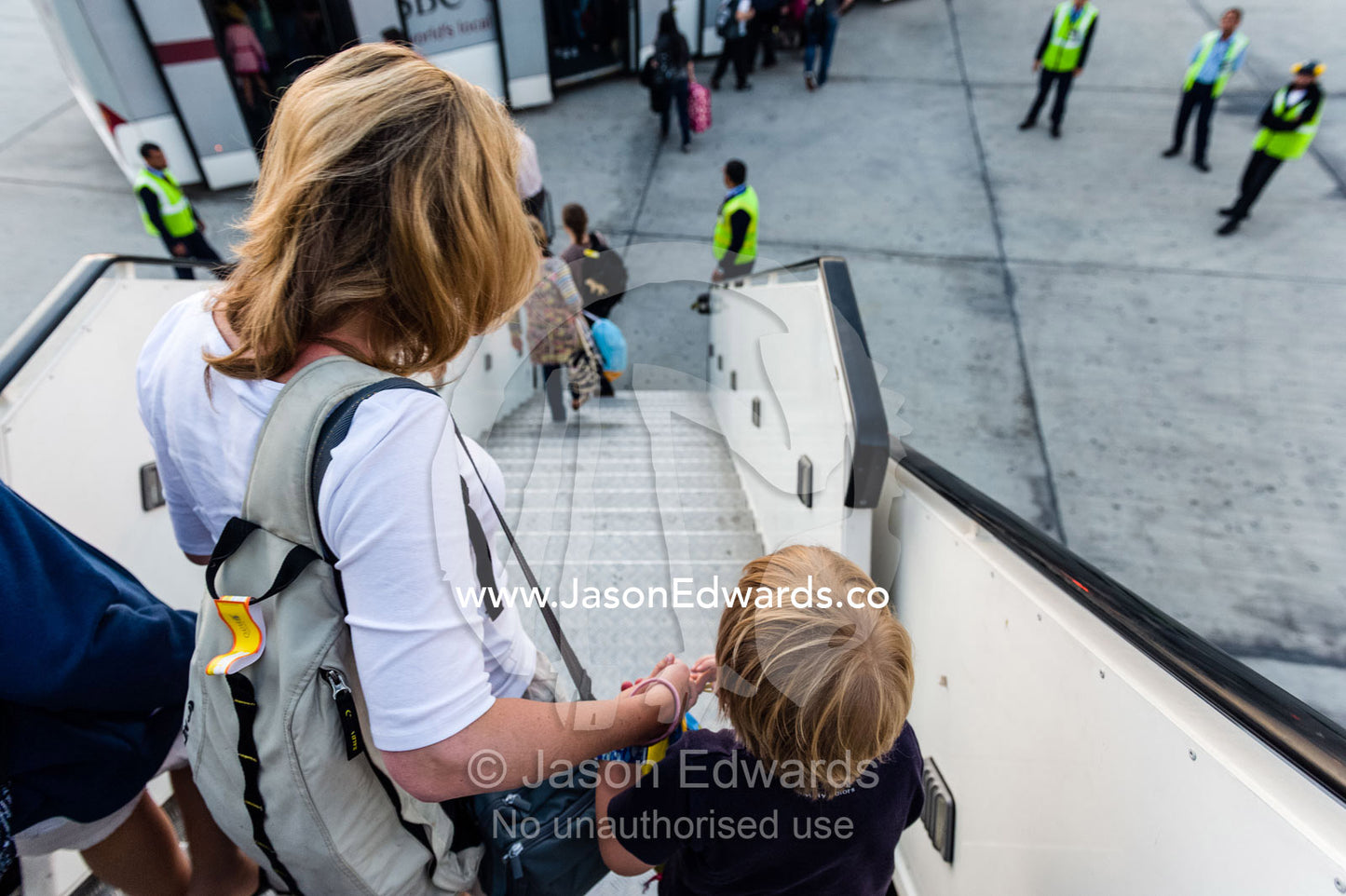 A mother assists her small son down the stairs from an aircraft onto the tarmac. Doha, Doha International Airport, Qatar.