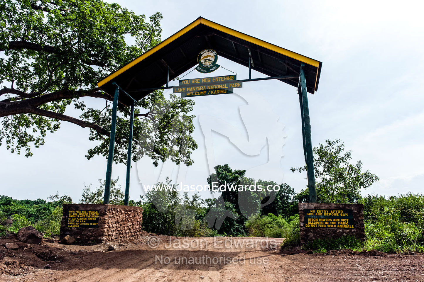 A dirt road passes through the entrance gate to Lake Manyara National Park. Karatu, Lake Manyara National Park, Arusha Region, Tanzania, Africa.
