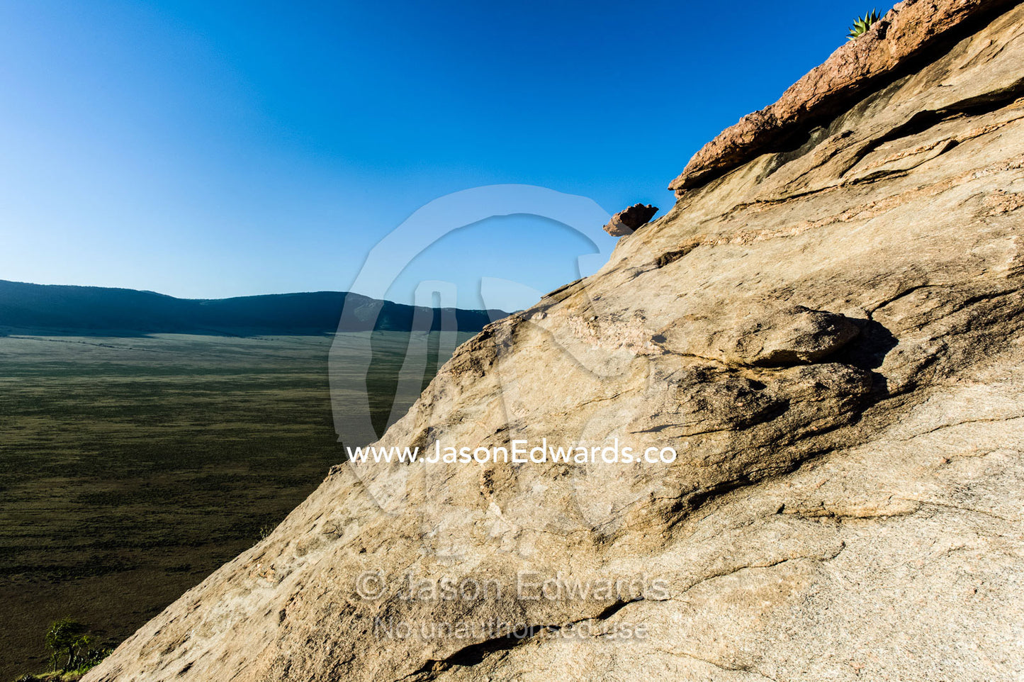 The steep eroded slope of a rock outcrop high above a savannah plain. Arusha, Nasera Rock, Angata Kiti Valley, Ngorongoro Conservation Area, Crater Highlands, Tanzania.