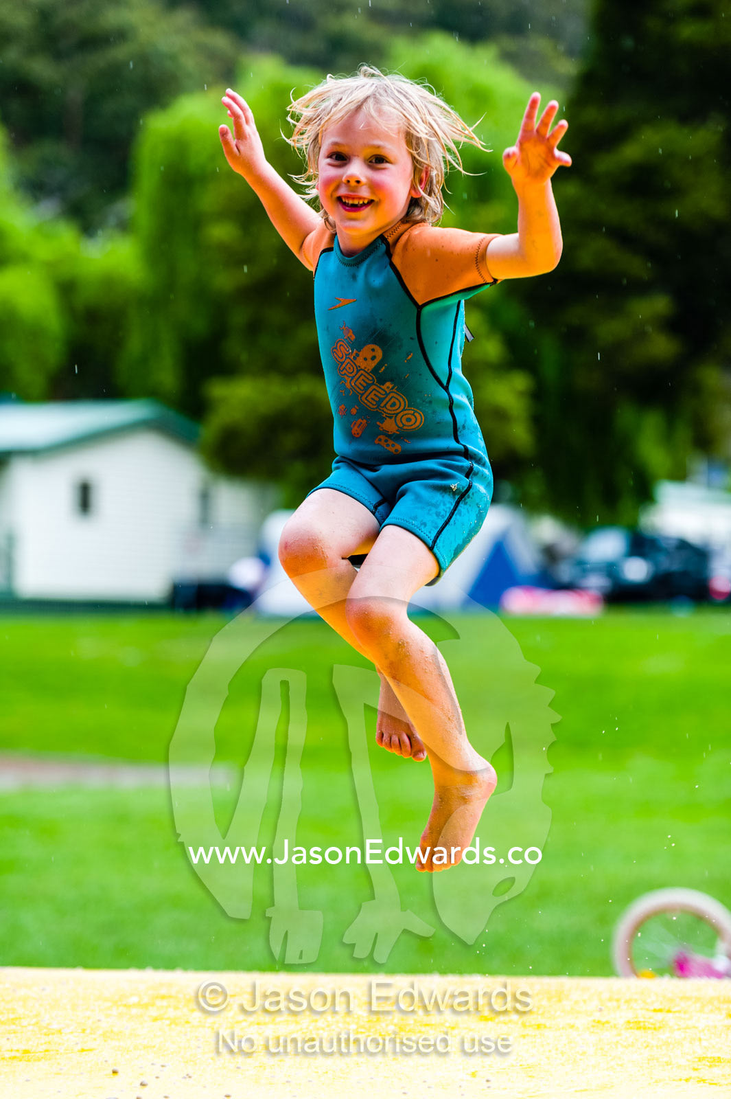 A boy laughing and jumping on an inflatable cushion in a wetsuit. Wye River, Great Ocean Road, Victoria, Australia.