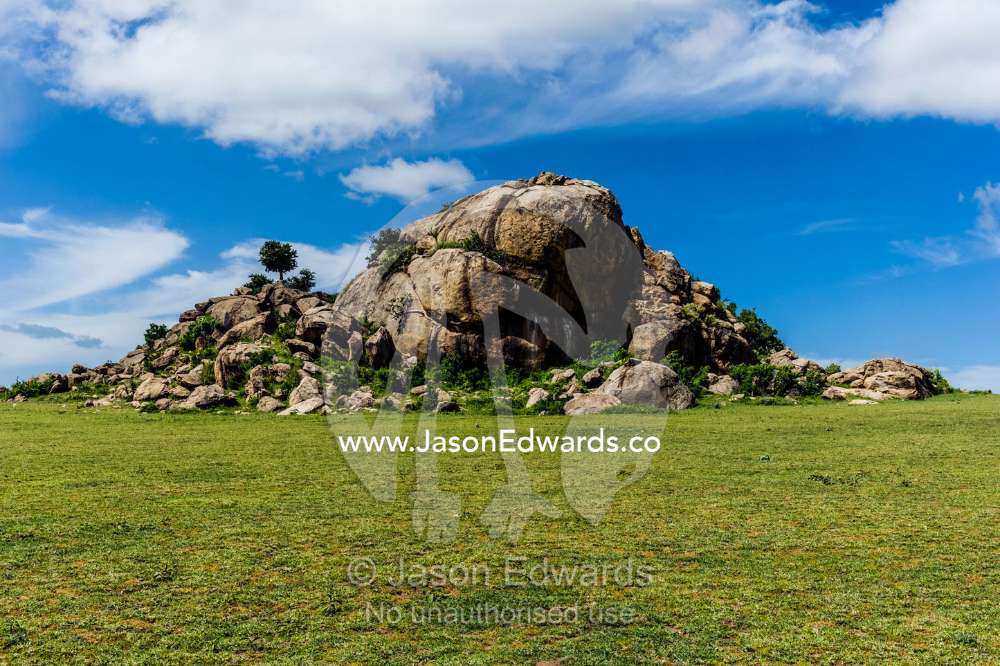 A tumble of granite boulders known as a kopje rises over the savannah plain. Ngorongoro Conservation Area, Ngorongoro District, Tanzania.