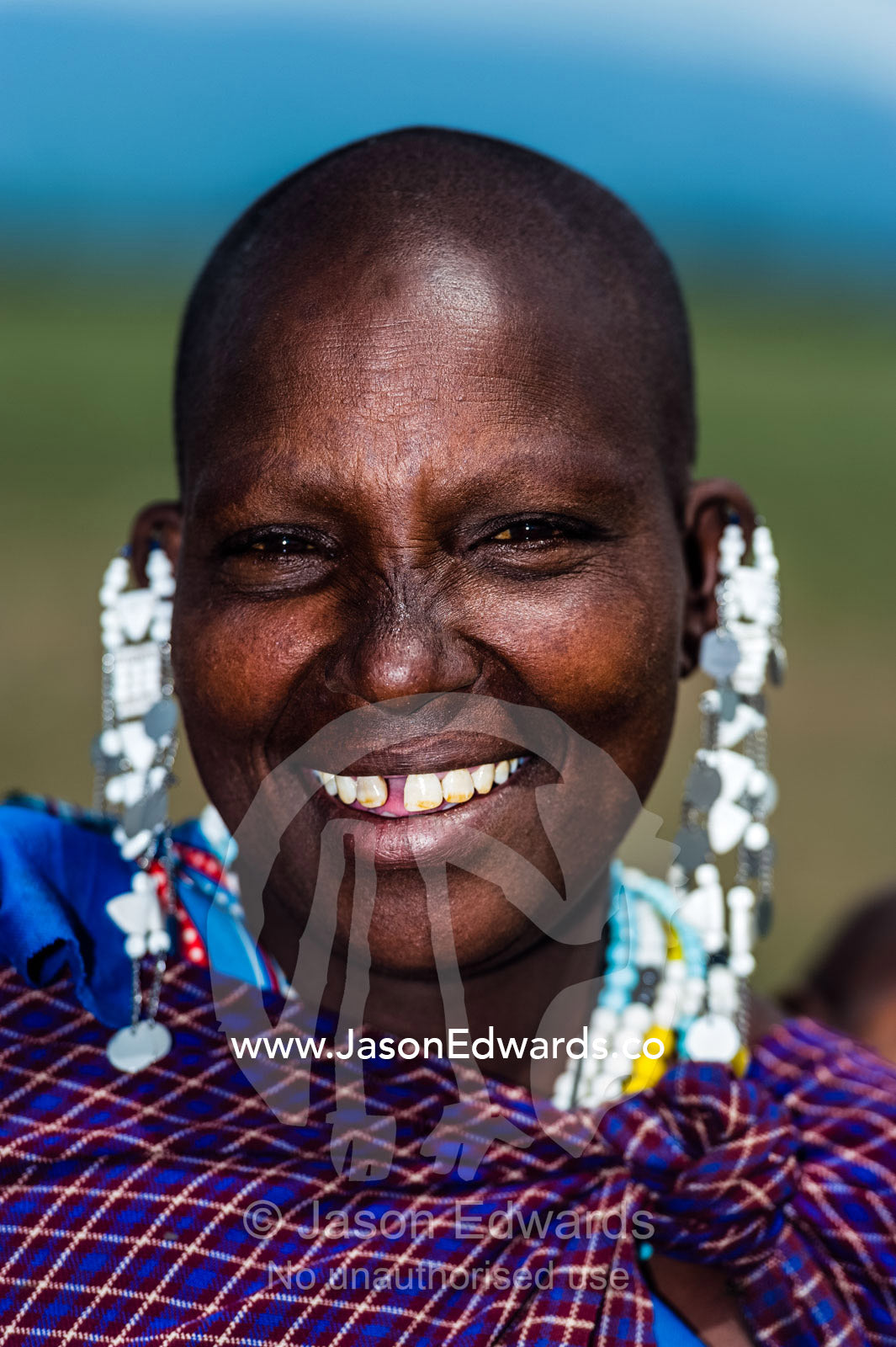 The happy, smiling face of a young Maasai woman with her head shaved. Ngorongoro Conservation Area, Ngorongoro District, Tanzania, Africa.