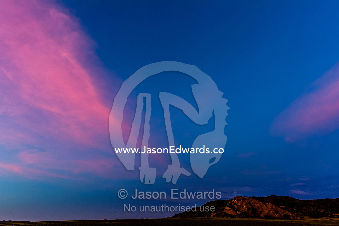 A pink flaming wisp of cloud hangs over a granite outcrop on the savannah horizon. Arusha, Nasera Rock, Angata Kiti Valley, Ngorongoro Conservation Area, Crater Highlands, Tanzania, Africa.