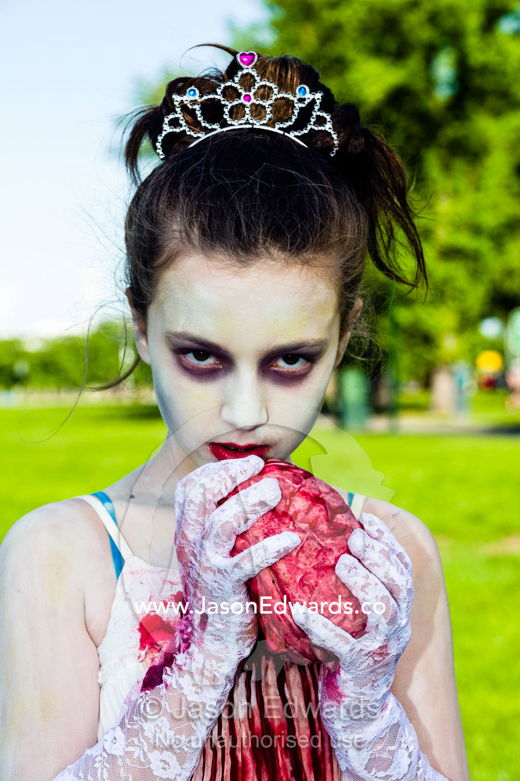 A girl dressed as a princess chews on a bloody heart at a zombie festival. Queen Victoria Gardens, Royal Botanic Gardens, South Yarra, Melbourne, Victoria, Australia.